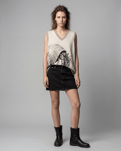 Model wearing light beige sleeveless knit vest with hermit crab design styled with high-waisted black denim mini skirt