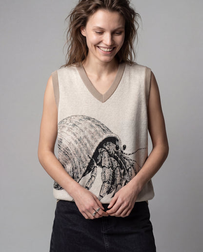Light beige knit vest with V-neck and ribbed trim featuring a large knitted hermit crab graphic emerging from lower torso