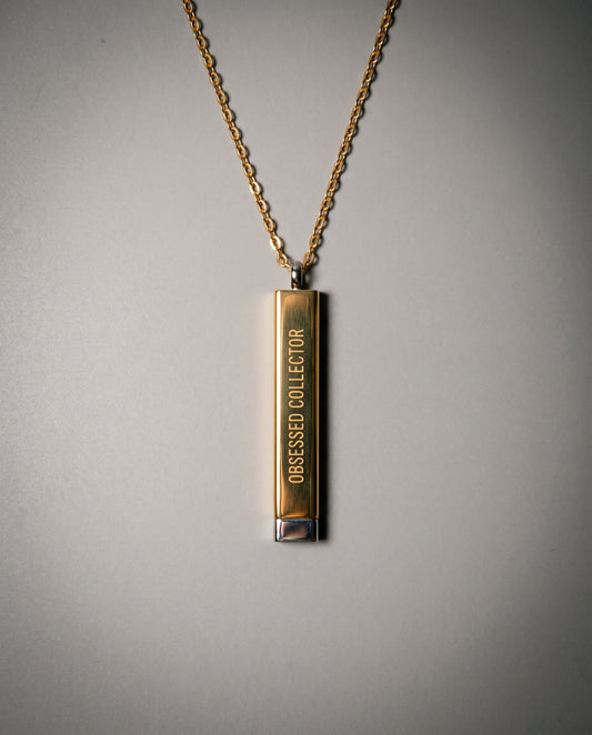 Gold-toned sliding bar necklace with 'OBSESSED COLLECTOR' engraving and silver cap