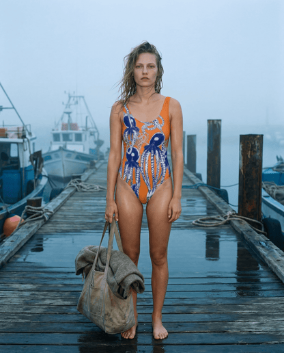 Orange octopus print one-piece swimsuit with scoop neck and high legs on wooden dock